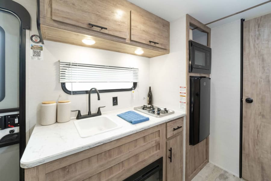 Compact RV rental kitchen: sink, two-burner stove, microwave, and fridge. Essential amenities for comfortable travel cooking.