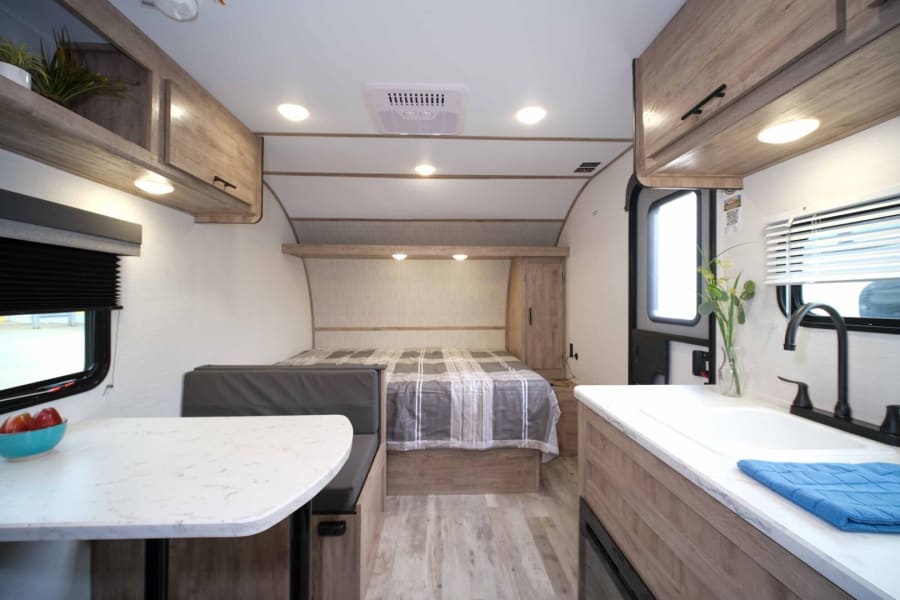 Discover this modern rv rental's interior with a comfortable bed, dinette, and compact kitchen area for travel.