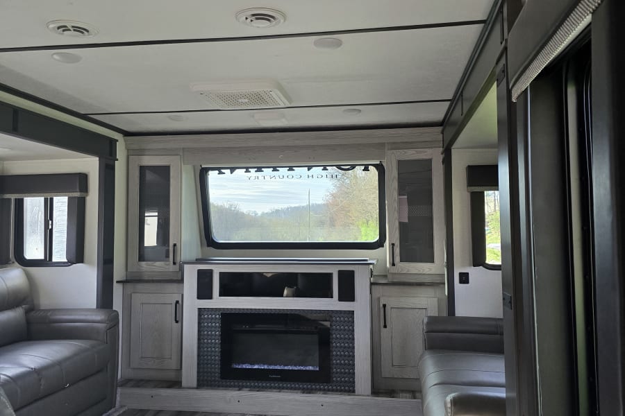 Inviting RV rental living space featuring comfy recliners, a fireplace, and a large window for outdoor views.