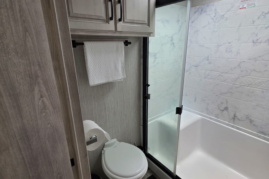 Compact RV rental bathroom: shower, toilet, cabinets, and skylight. Enjoy practical amenities for your travels.