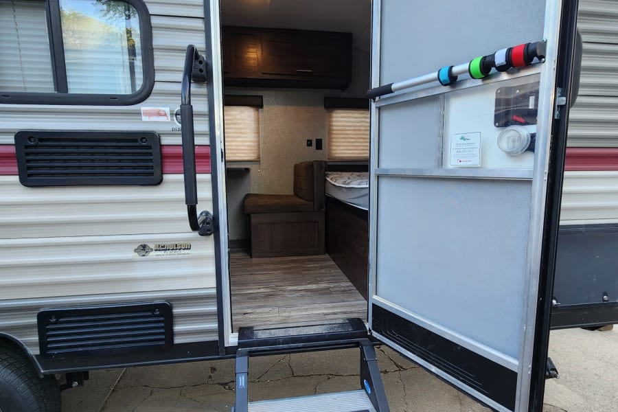 RV rental showing an open entry door with extended steps, revealing a glimpse of the interior, ready for camping travel.