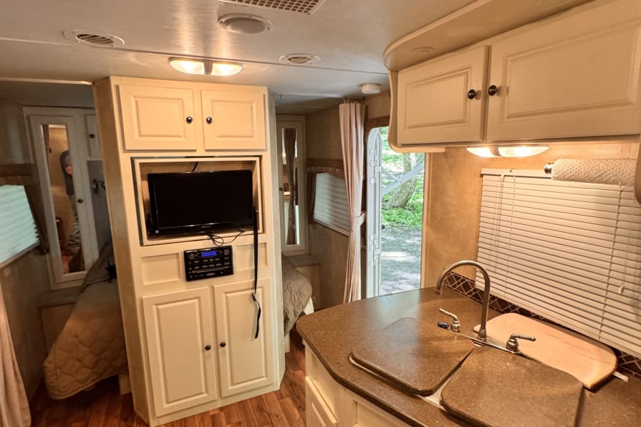 Inside this RV rental, find a full kitchen, living space with TV, and cozy bedroom. Perfect amenities for your next adventure.