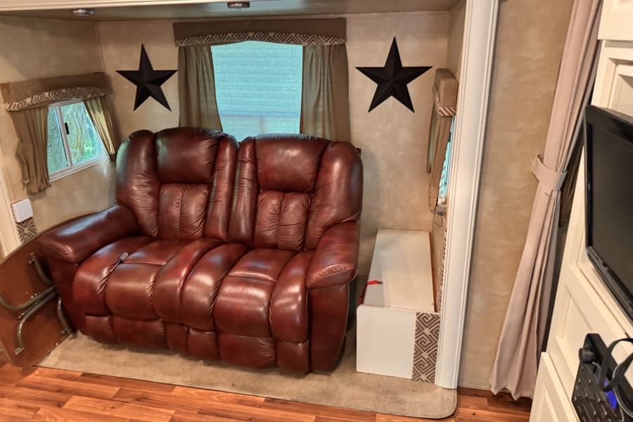 Inside a comfortable **RV rental**: brown leather recliner sofa, decorative stars, and windows with curtains.