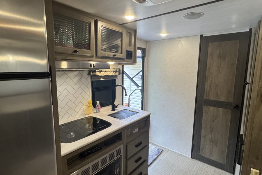 Experience comfort in this RV rental's modern kitchen: fridge, cooktop, microwave, stylish cabinets, and bright, clean design.