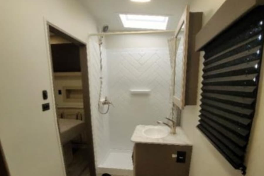 This RV rental bathroom features a compact shower, vanity sink, and toilet. Skylights brighten this functional space.