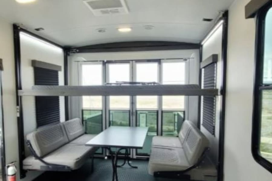 Functional RV rental toy hauler interior: dining table, convertible bench seating, and an overhead bunk bed.
