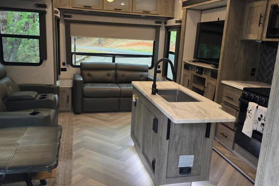 Spacious RV rental interior with living area, kitchen island, and herringbone flooring for comfortable travels.