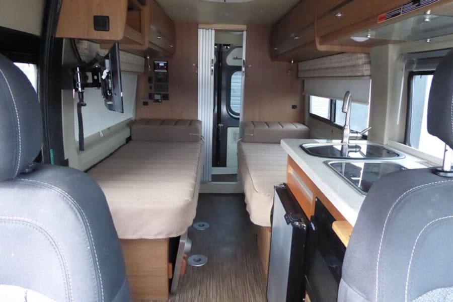 RV rental interior showing twin beds, kitchen with sink, mounted TV, and overhead cabinets for a comfortable camper van experience.