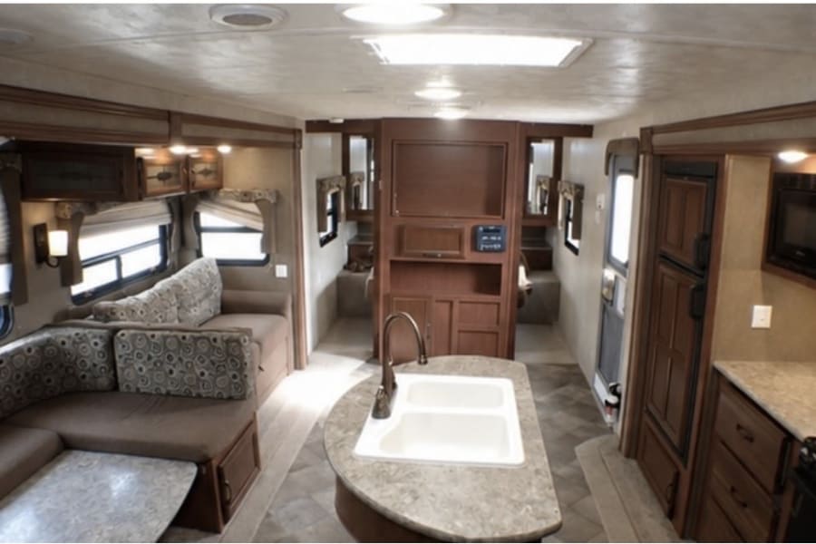 Spacious RV rental interior: U-shaped dinette, kitchen island with sink, fridge, microwave, and rear bunk beds.