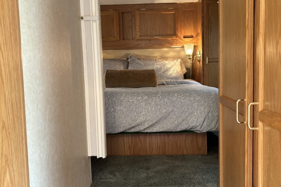 Cozy RV rental bedroom with carpeted steps, a comfortable bed, and warm wood cabinetry.