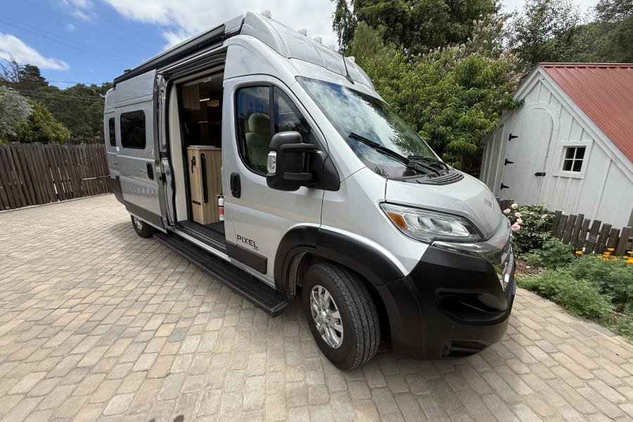 Silver Pixel RV rental camper van parked on a paved driveway, its side door open to reveal the interior.