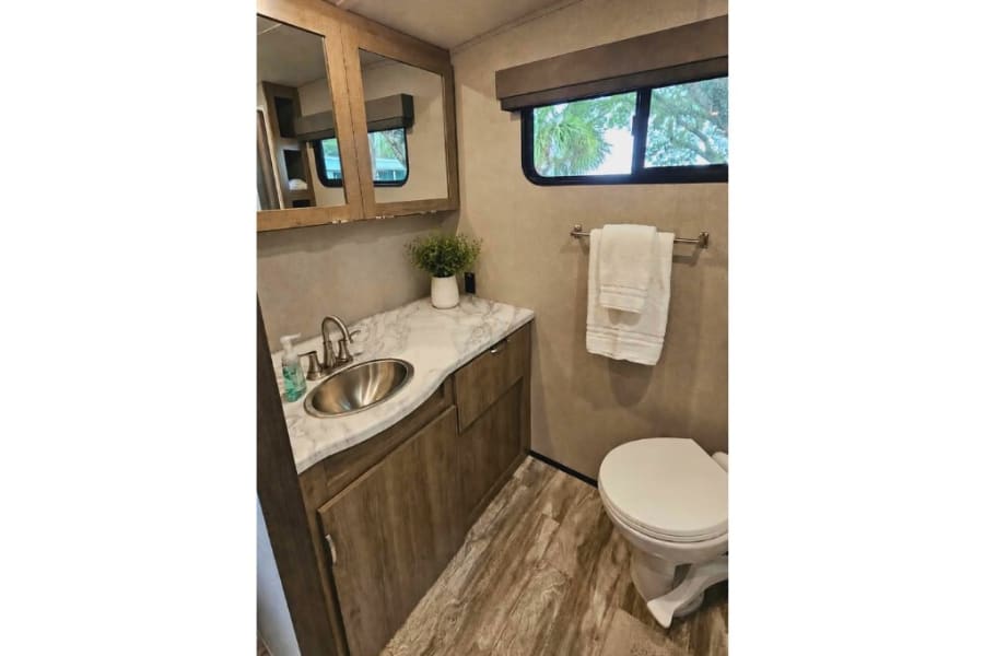 This modern RV rental bathroom features a vanity, sink, mirror, toilet, and clean towels.