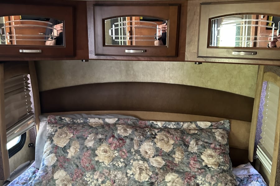 Cozy RV rental bedroom featuring floral bedding, a brown headboard, and mirrored overhead storage cabinets for a comfortable stay.