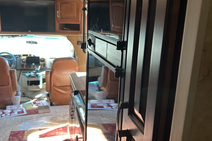 RV rental interior: View from the living area towards the front cockpit. A reflective refrigerator door is on the right.