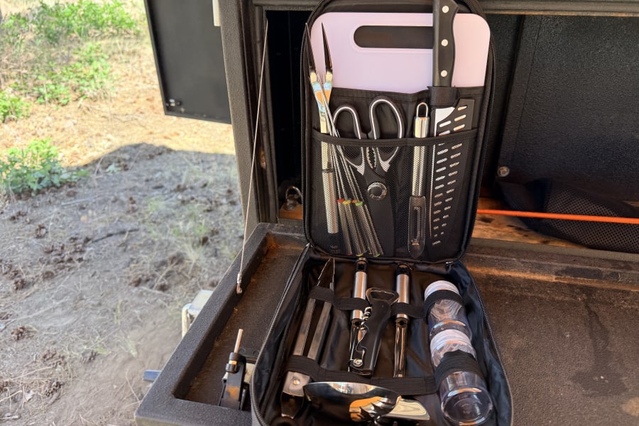 RV rental portable kitchen kit: Organized with knives, cutting board, spices, and various cooking utensils.