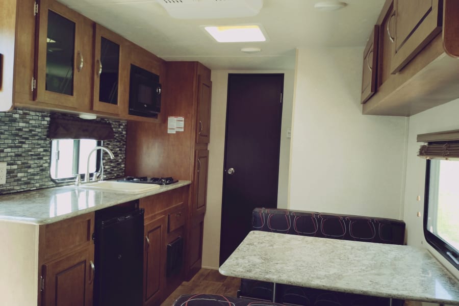 RV rental interior: a modern kitchen with sink, stovetop, microwave, fridge, wood cabinets, and a cozy dining booth.