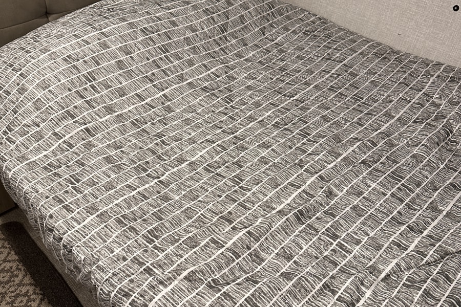 Cozy RV rental interior featuring a neatly made bed with a striped comforter and an emergency exit window.