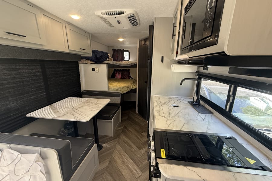 Modern RV rental interior with a bright kitchen, dining area, and bunk beds. Enjoy comfortable living in this stylish camper.