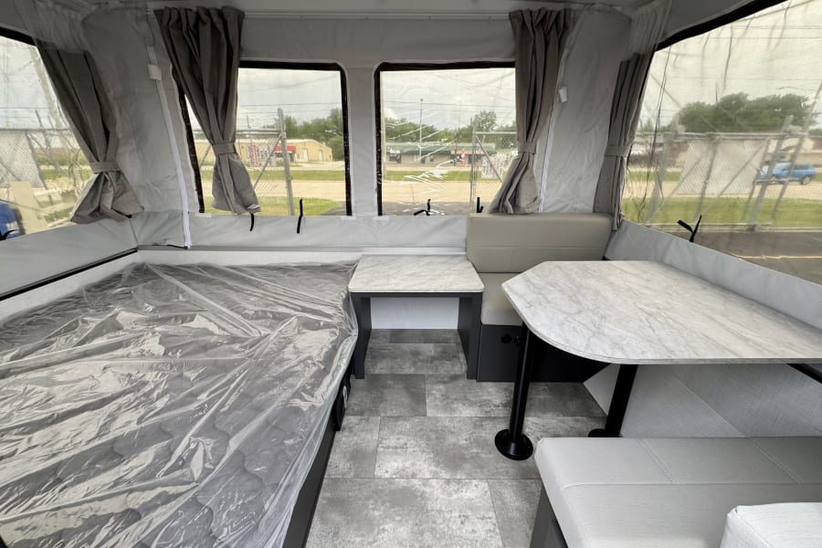 Modern RV rental interior: a clean pop-up camper with a protected bed, dinette seating, and large windows.