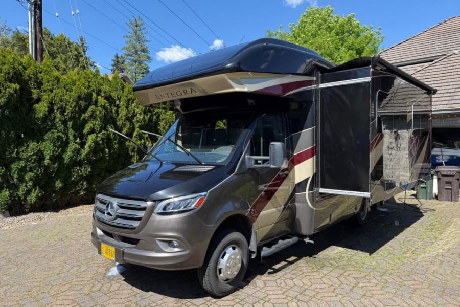 Ready for adventure! A luxurious brown Entegra Mercedes-Benz Sprinter RV rental with its awning extended on a sunny day.