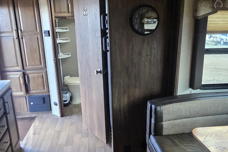 Inside a spacious RV rental, highlighting the dinette, open bathroom, wood cabinetry, wood-look floor, and ceiling AC unit.