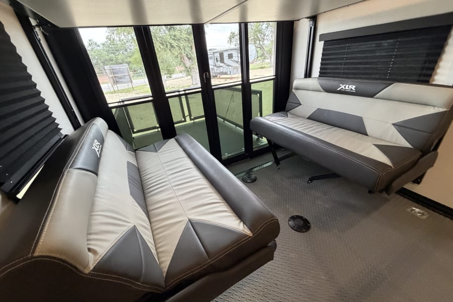 RV rental interior: Modern toy hauler with two-tone convertible benches, large rear glass doors, and diamond plate flooring.