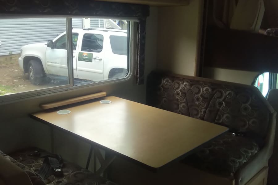 RV rental dinette interior: cozy seating, table, overhead storage, and 'Adventurer' paddle decor for your next road trip.