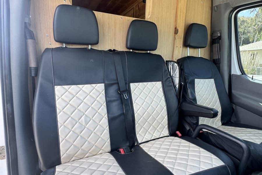 RV rental interior showcasing stylish black & white quilted seats. Wood paneling & ceiling vent visible in the campervan.