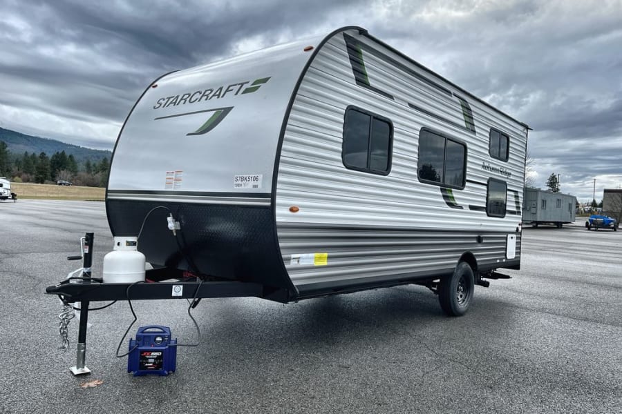 Grey Starcraft Autumn Ridge travel trailer, an excellent RV rental, parked on asphalt with mountains and cloudy sky.