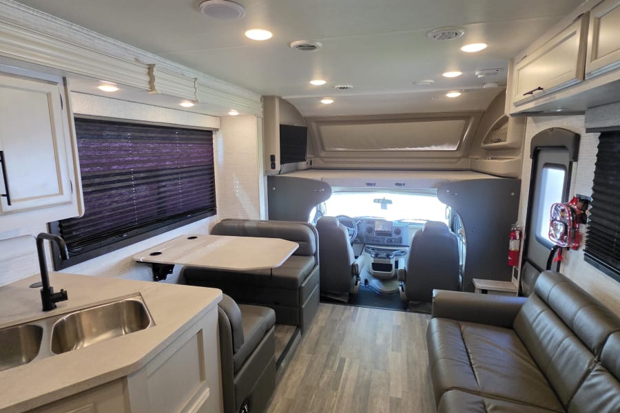 A bright, modern rv rental interior showcasing a kitchen, dinette, couch, and driver's area with sleek finishes.
