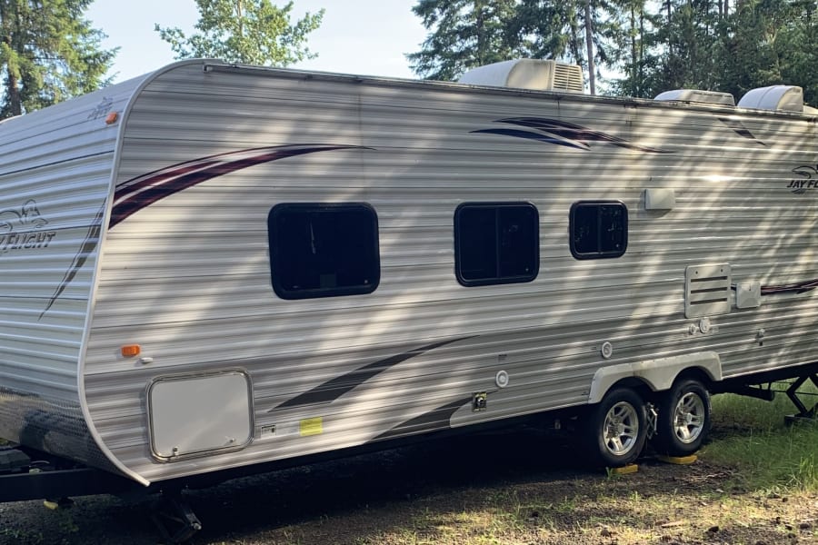 A grey and white Jayco Jay Flight travel trailer RV rental, parked in a wooded area, ready for your next adventure.