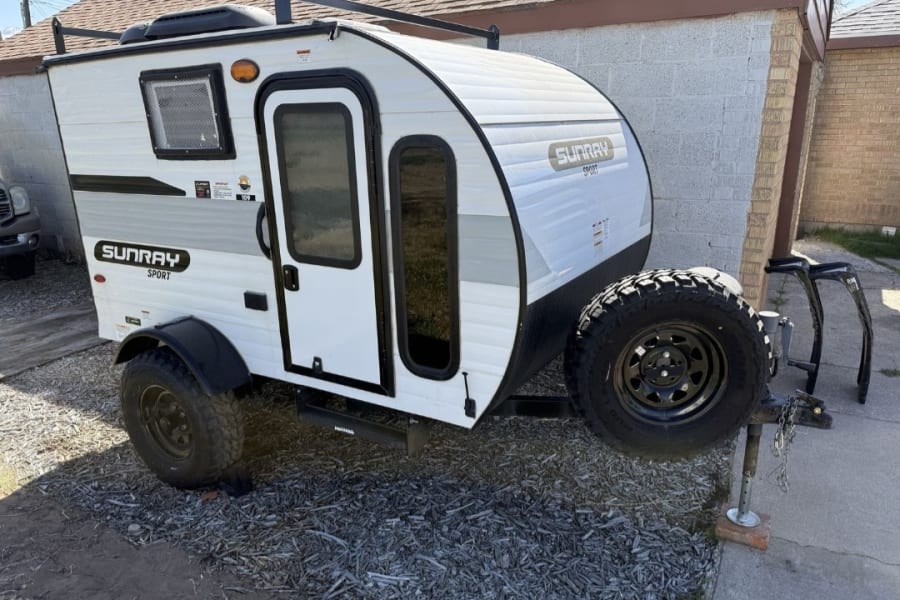 White Sunray Sport teardrop camper with off-road tires & roof rack, ideal for an RV rental adventure or camping.
