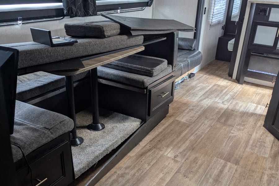 RV rental interior featuring a modern dinette with gray seating, black cabinetry, and wood-look flooring.