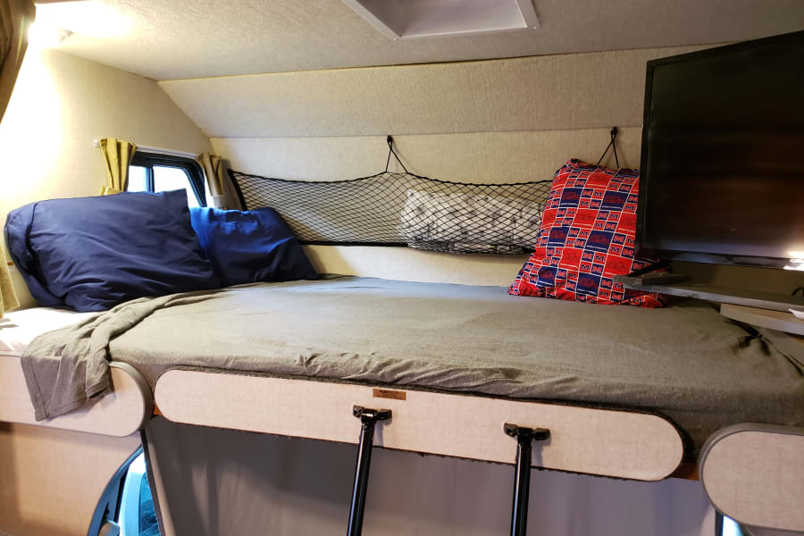 Over cab bunk area is outfitted with 2 twin mattresses.  Step ladder hooks into panel for safe movement from the living area to the bunk.  Storage is provided at the foot of the bed.  The TV can be rotated for guests to enjoy a movie while relaxing. 