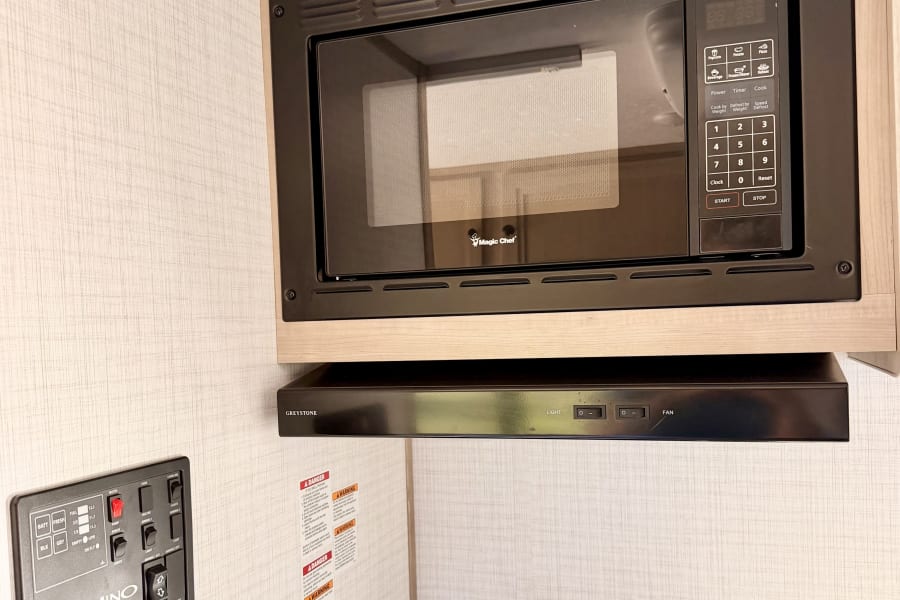 Inside an rv rental: Kitchenette features a Magic Chef microwave, stovetop, Greystone hood, & Palomino control panel.