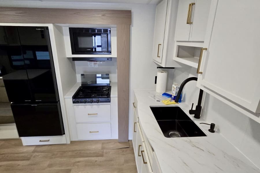Modern RV rental kitchen featuring white cabinets, black appliances, marble counters with a black sink. Clean, bright interior.