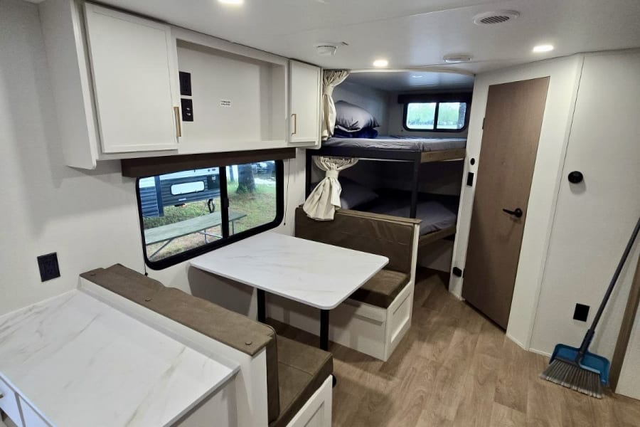 RV rental interior: cozy dining booth, compact kitchen, and bunk beds for family travel.
