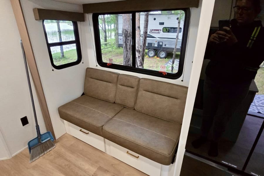 This RV rental interior features a dinette bench with storage, scenic windows overlooking a lake, and light wood floors.