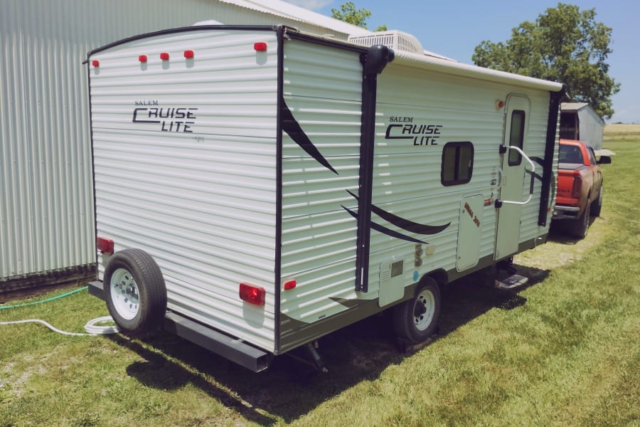 White Salem Cruise Lite rv rental travel trailer with a spare tire on the back, parked on green grass outdoors.