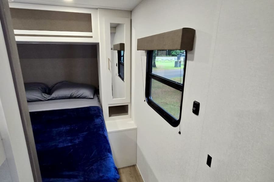Bright RV rental interior features modern bunk beds, a window overlooking nature, and efficient compact design.