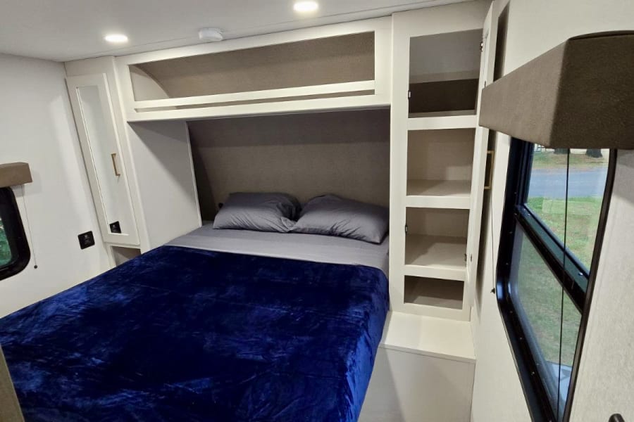 Cozy RV rental bedroom with a bed, overhead storage, and window. Ideal for comfortable travel accommodations.