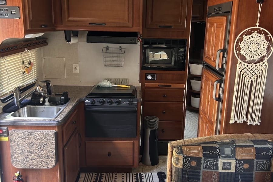 Well-equipped RV rental kitchen featuring a sink, stove, microwave, and refrigerator, complete with wood cabinets and seating area.