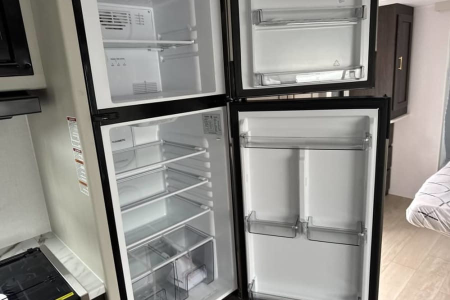 Inside an RV rental: a clean, empty two-door refrigerator/freezer, ready for your trip. Shelves and door bins are visible.