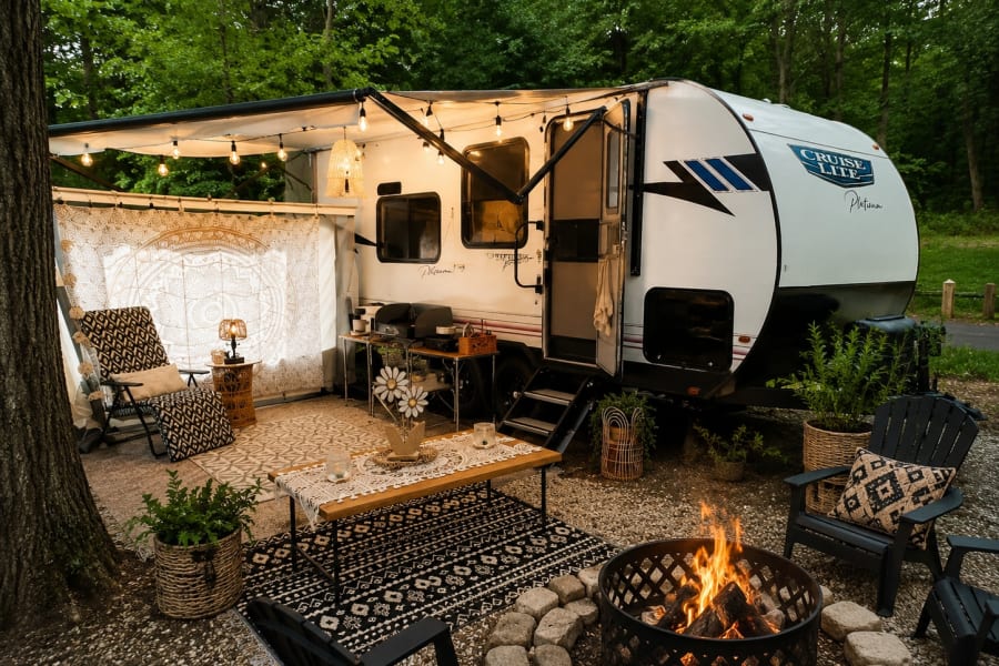 An inviting rv rental campsite setup with a camper, fire pit, cozy seating, rugs, and string lights creating an outdoor living space.