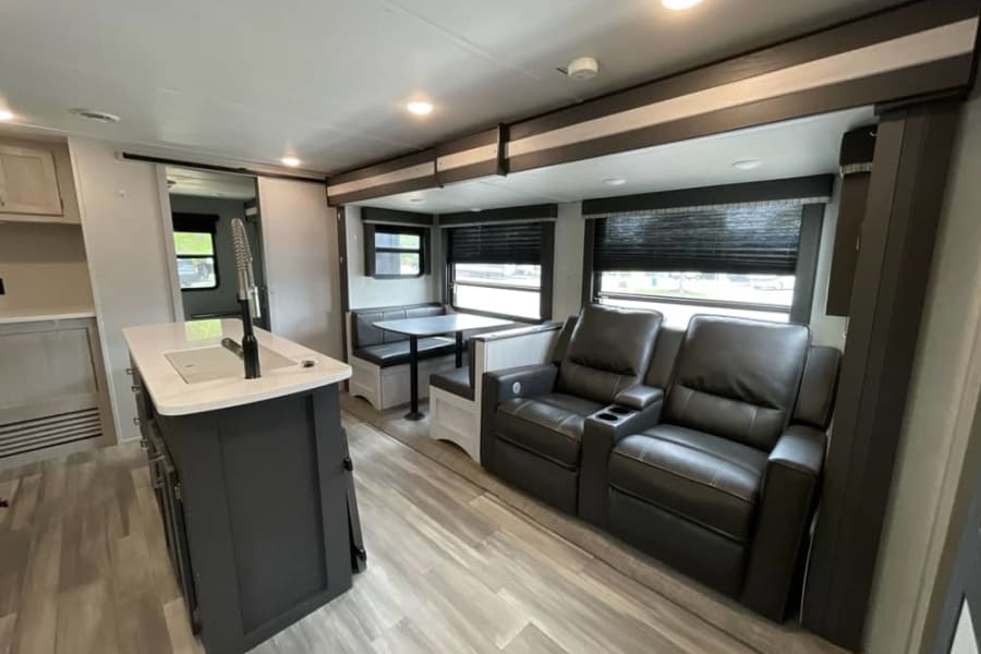 Spacious RV rental interior with a modern kitchen island, dining booth, and comfortable recliner sofa.