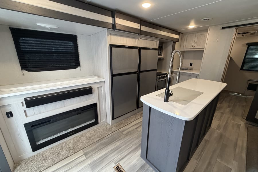 Modern RV rental interior featuring a full kitchen with an island, double fridge, and cozy living space with a fireplace.
