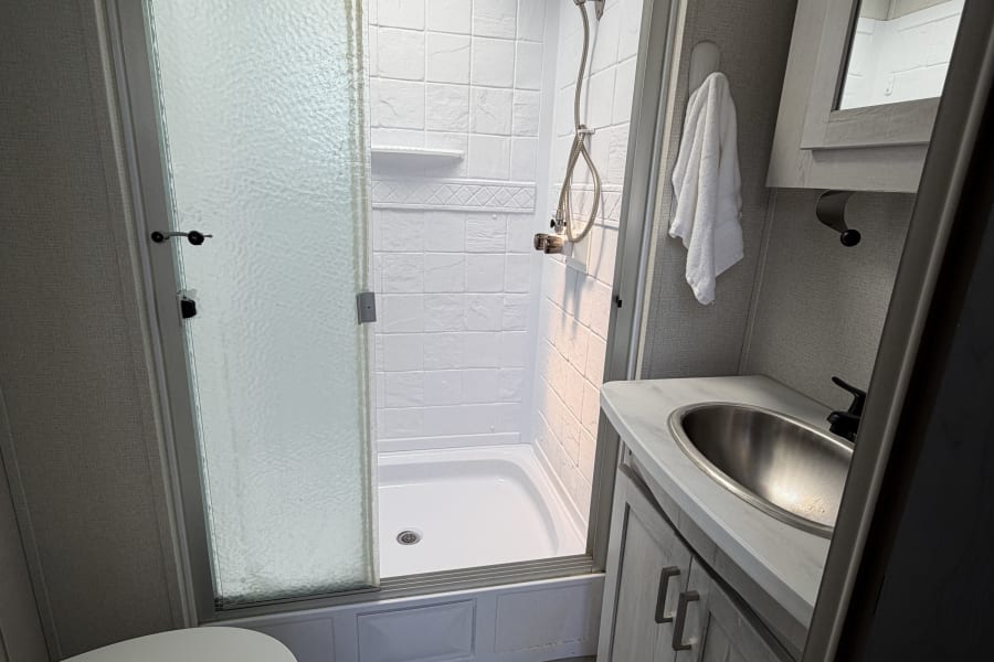 Compact RV rental bathroom: glass shower with skylight, toilet, and vanity with sink. Ideal for travel and camping comfort.