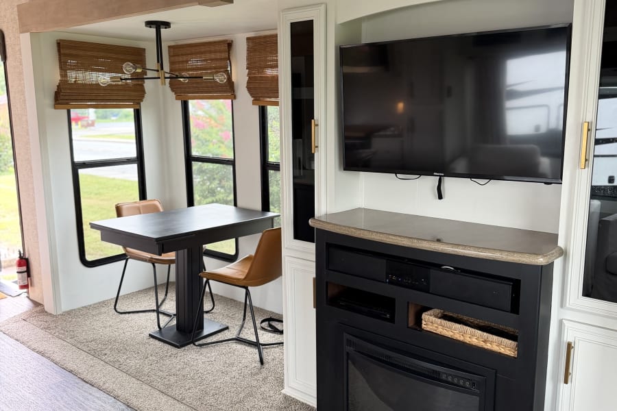 Cozy RV rental interior with a dining nook, built-in entertainment center, TV, and electric fireplace. Ideal for travel.