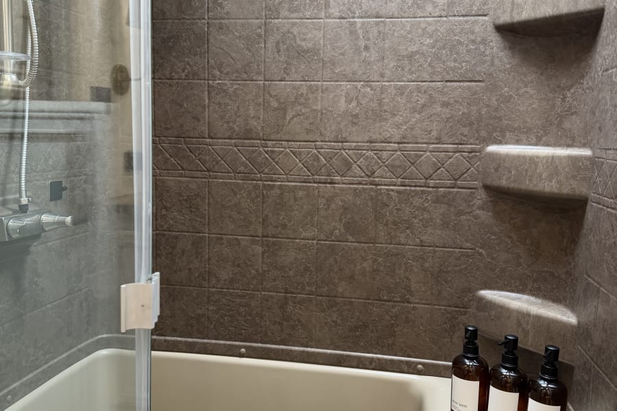 Inside an RV rental, a compact bathroom with a shower/tub combo, built-in shelves, and amenities in labeled dispensers.