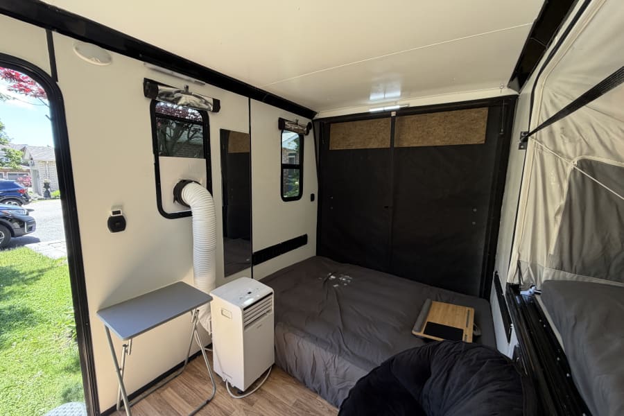 Cozy rv rental interior featuring a bed, portable AC, windows, and folding table. Ideal for compact living.